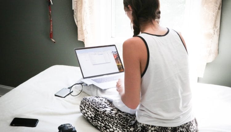 woman in white tank top sitting on bed in front of laptop computer