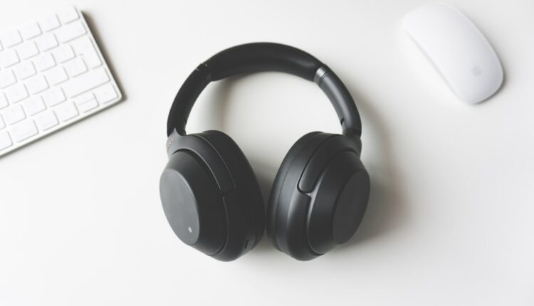 black wireless headphones between Apple Keyboard and Apple Magic Mouse on white surface