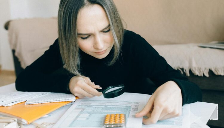 A focused young woman examines documents with a magnifying glass, highlighting attention to detail in accounting tasks.